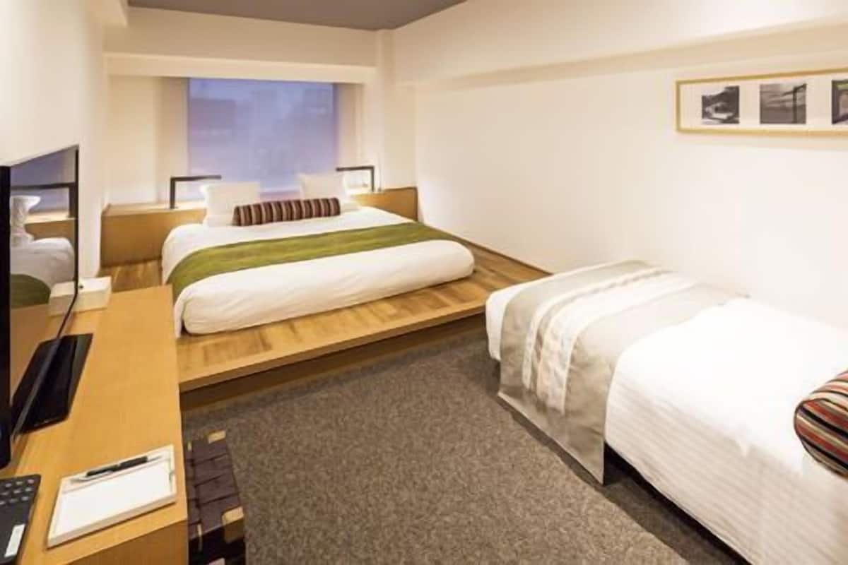 Ein Hotelzimmer mit einem Bett, einem Schreibtisch mit Computer, einem Fernseher und einem Fenster.