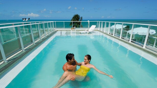 Una pareja en una piscina azul cristalina, con vistas al océano.