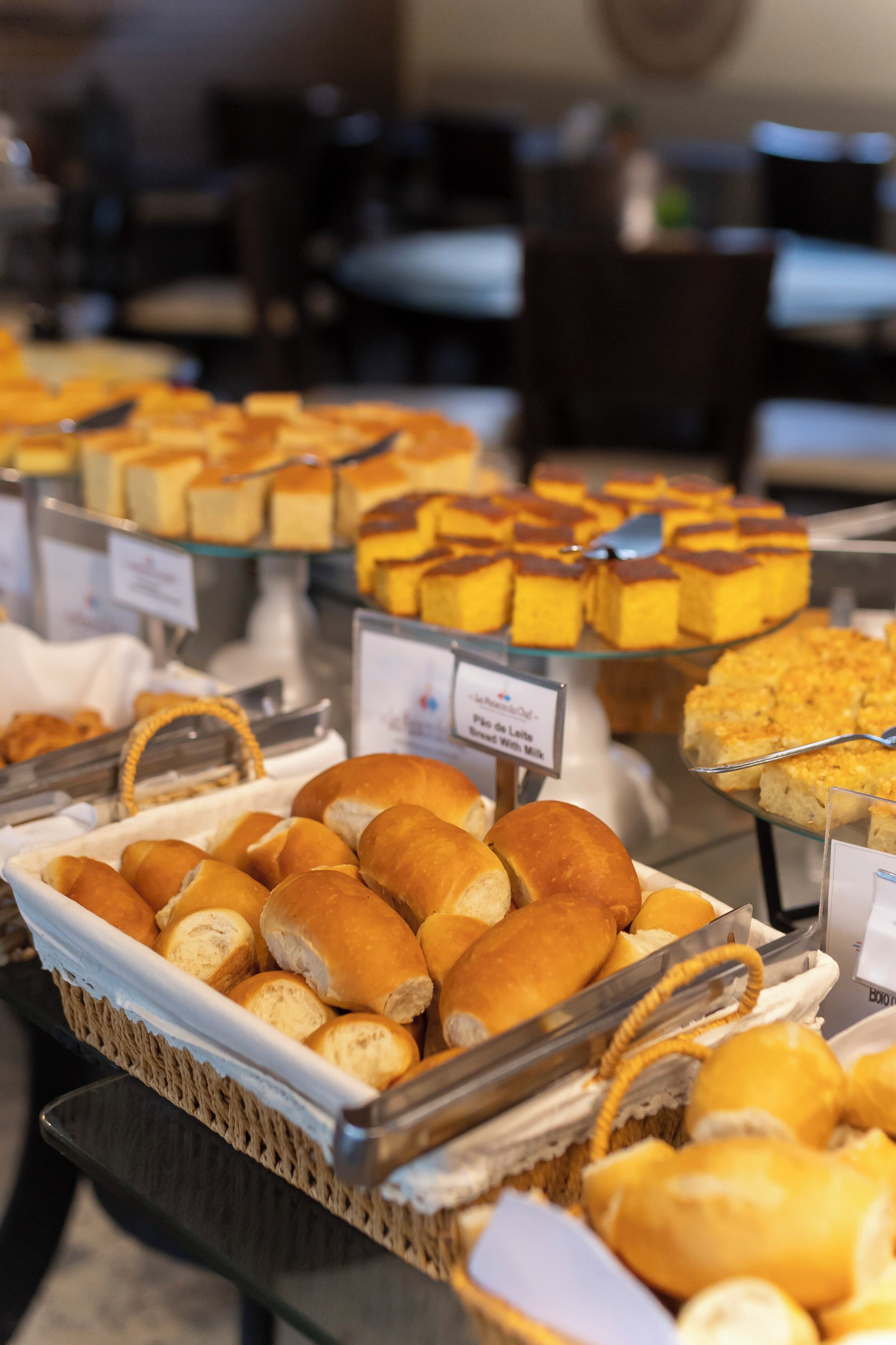 A buffet with various baked goods, including bread rolls and pastries, displayed in baskets and trays.