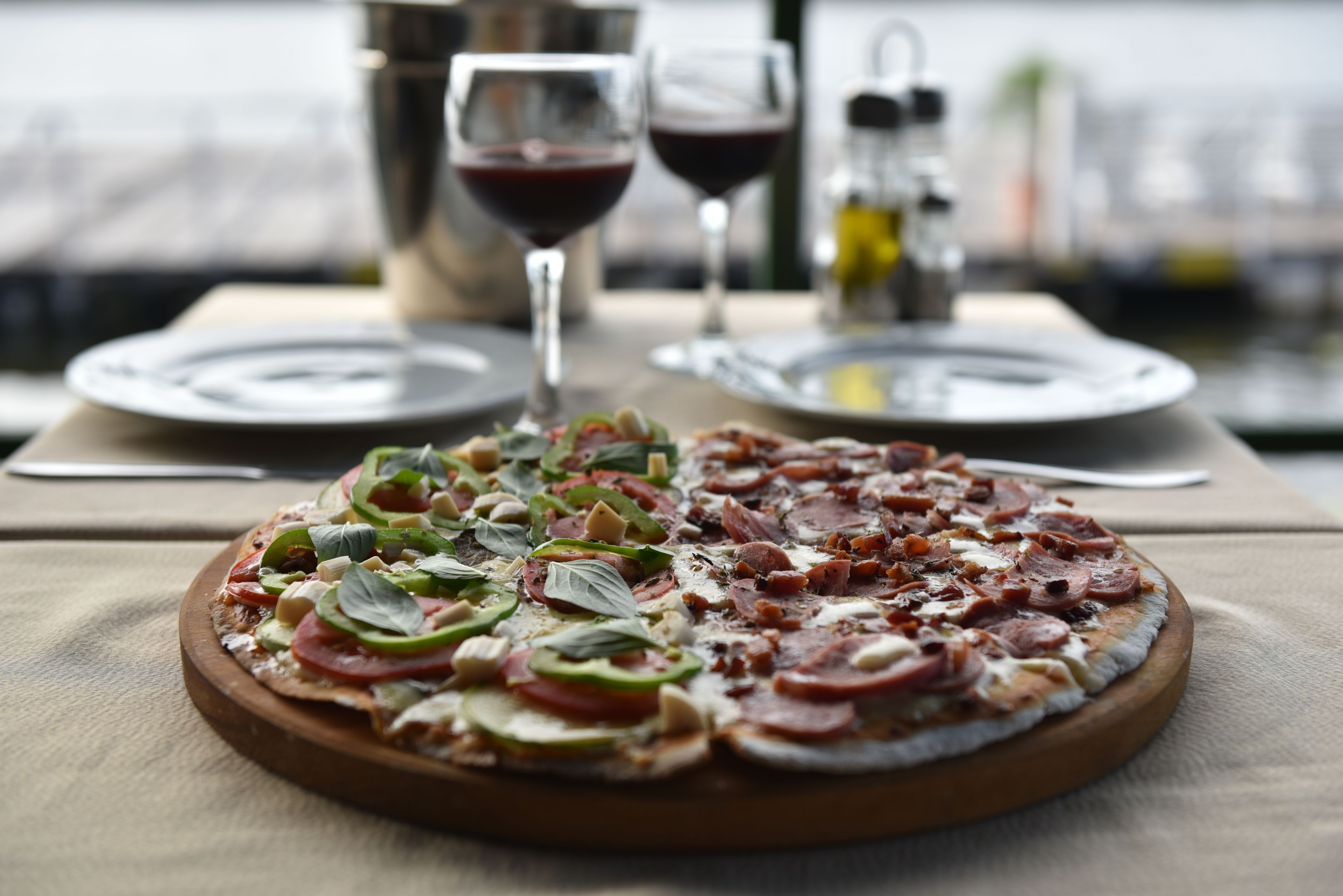 Une pizza servie sur une planche en bois, avec une table dressée en arrière-plan.