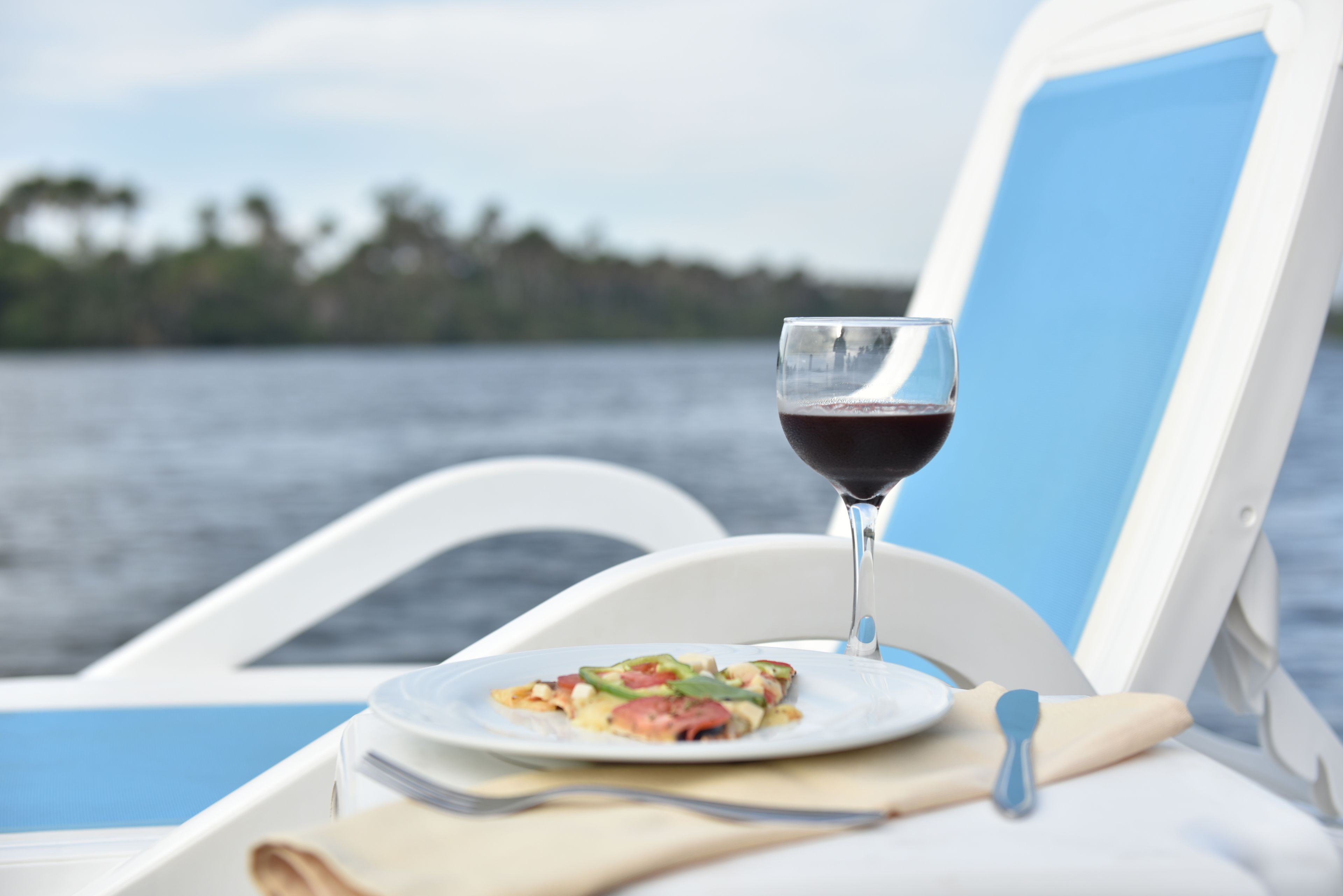Una mesa de comedor con un plato de comida y una copa de vino tinto en un barco.