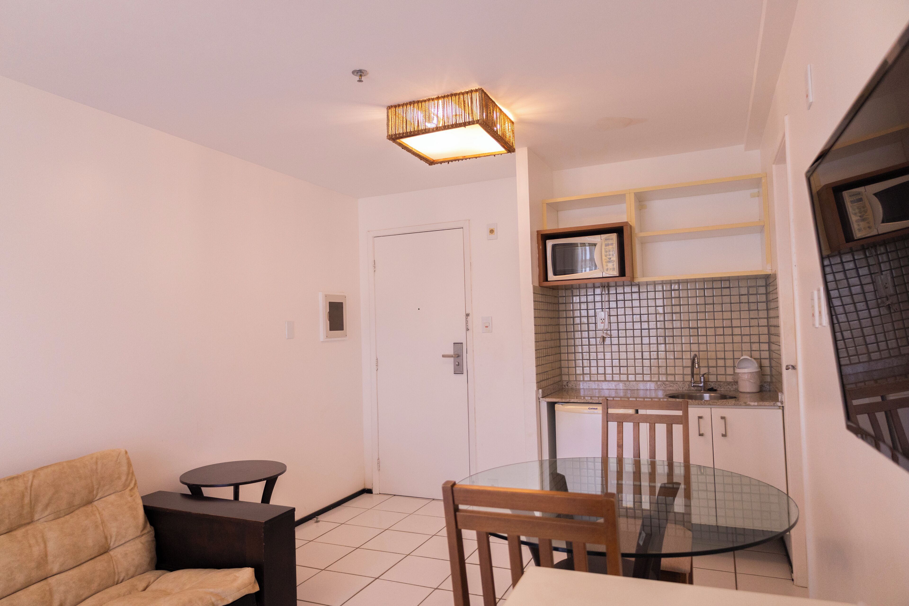 A compact living space with a kitchenette, a dining area with a glass table, a sofa, and a small round table.