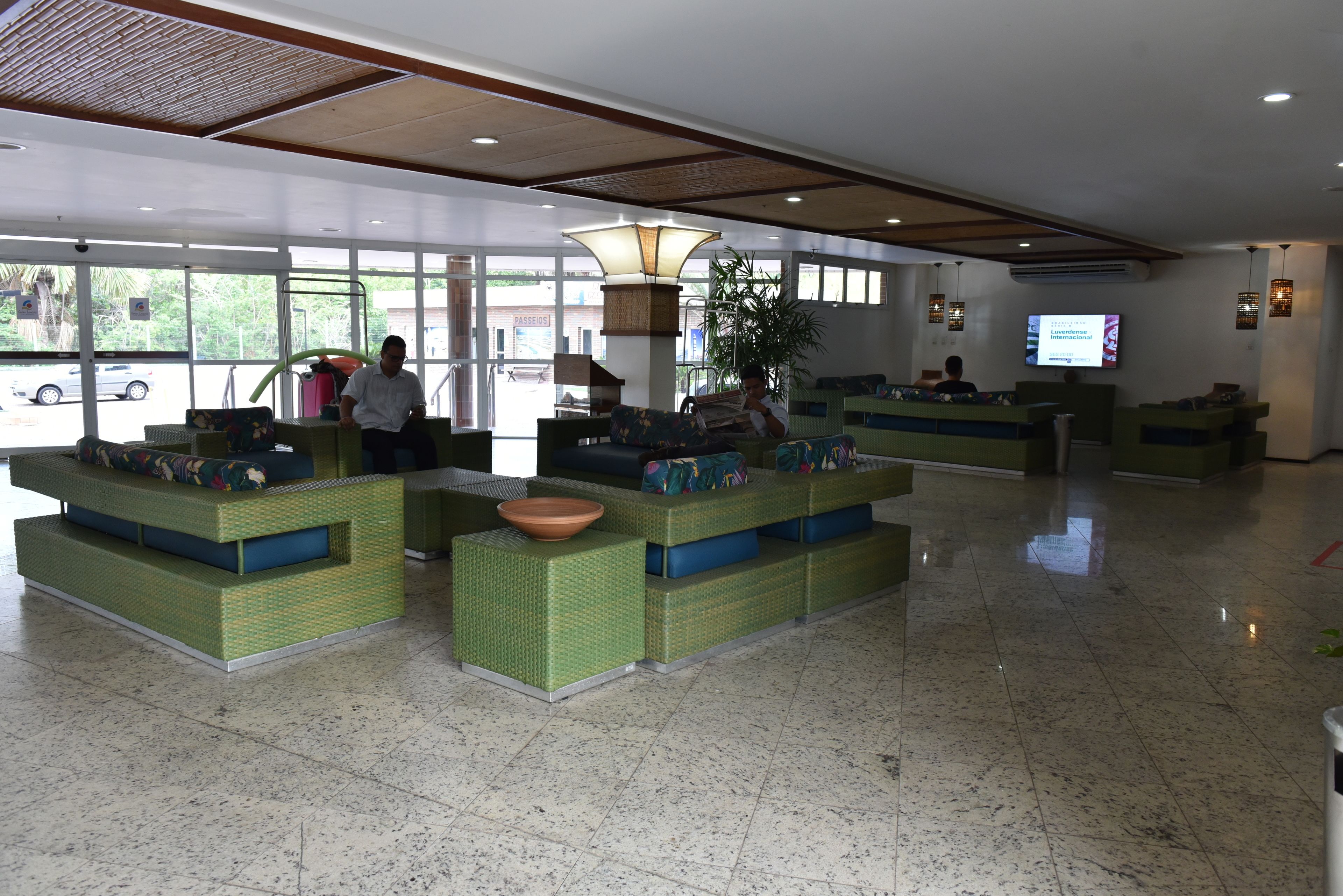 A spacious lobby with green seating areas, a large window, and a television screen.