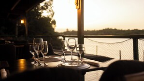 A table set for dining with wine glasses and plates, overlooking a body of water at sunset. - Hotel Gran Lençóis Flat (Barreirinhas)