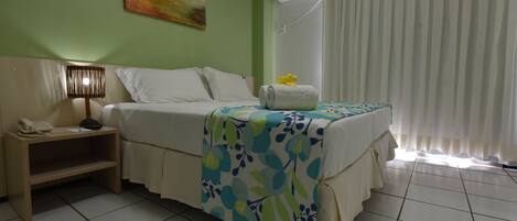 A hotel room with a bed, a nightstand with a lamp, a painting on the wall, and an air conditioning unit.