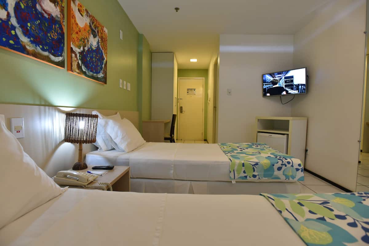 A hotel room with two beds, a TV mounted on the wall, and artwork on the walls.