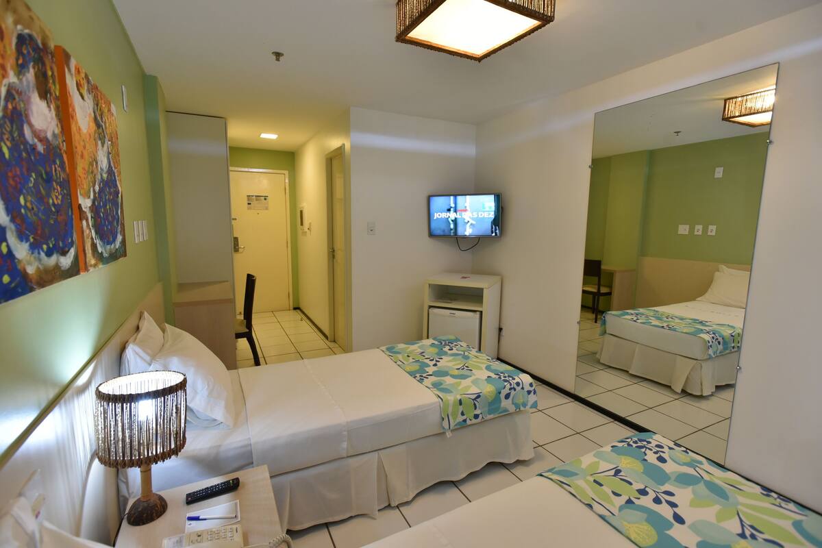 A hotel room with two beds, a TV, a bedside table, and a lamp.