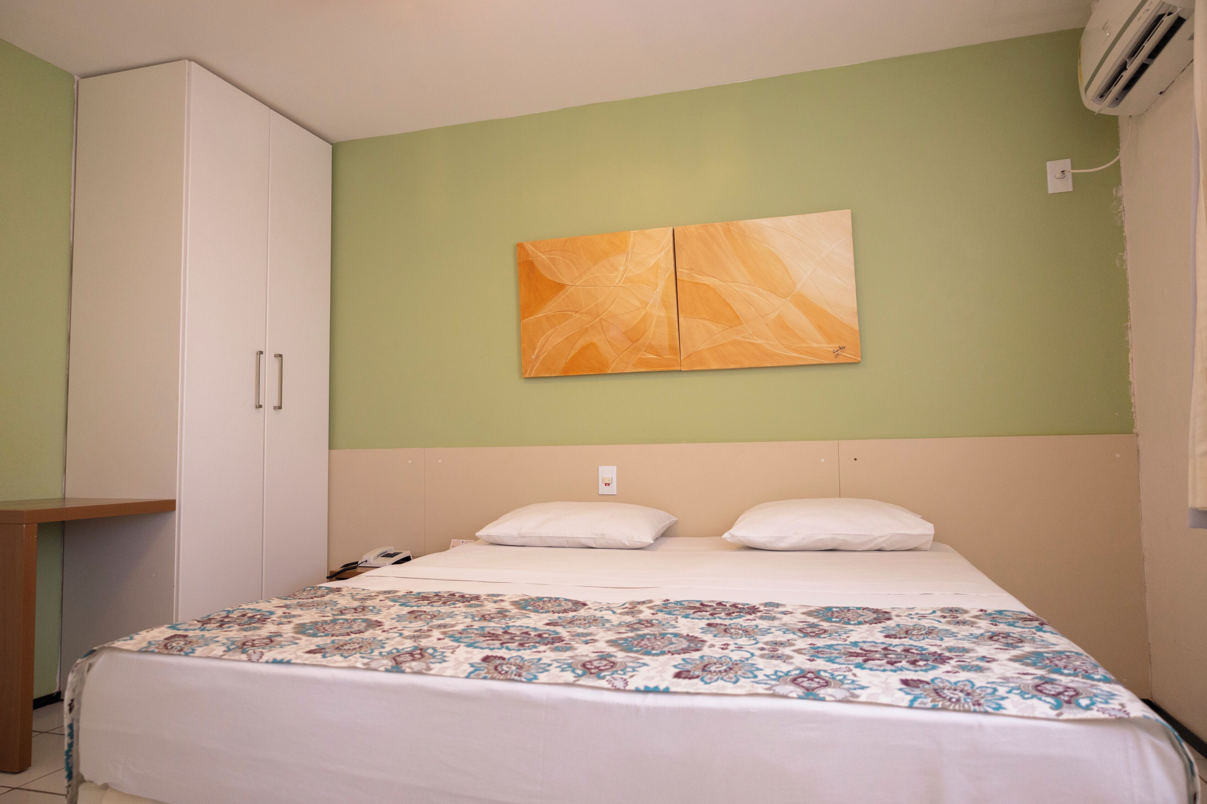 A bedroom with a bed, a wardrobe, a wall-mounted air conditioner, and a painting.