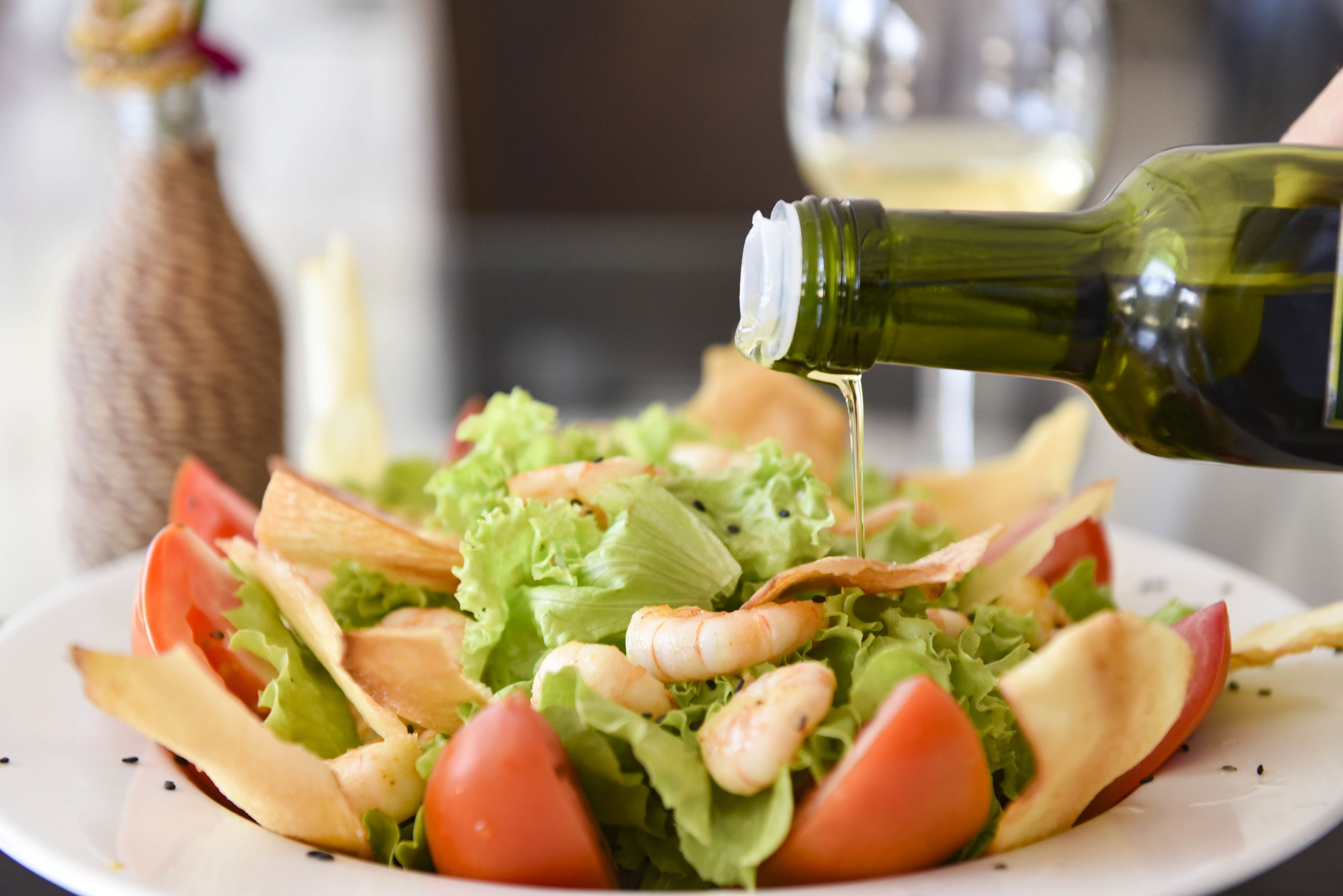 A plate of salad with lettuce, tomatoes, and shrimp, being drizzled with olive oil.