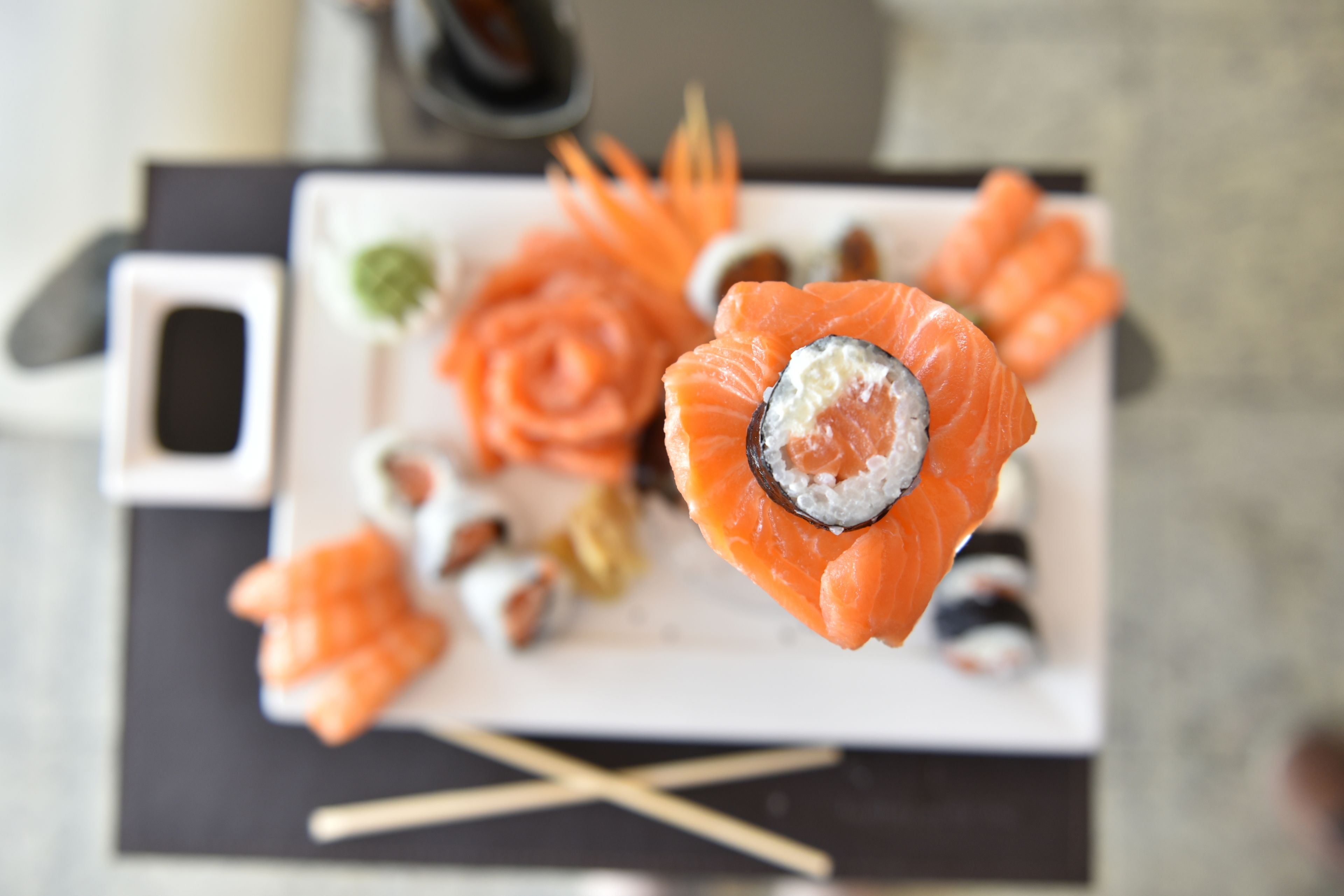 Une assiette de sushis variés, comprenant des nigiris et des sashimis, présentée sur une assiette blanche avec des baguettes et un petit récipient de sauce soja.