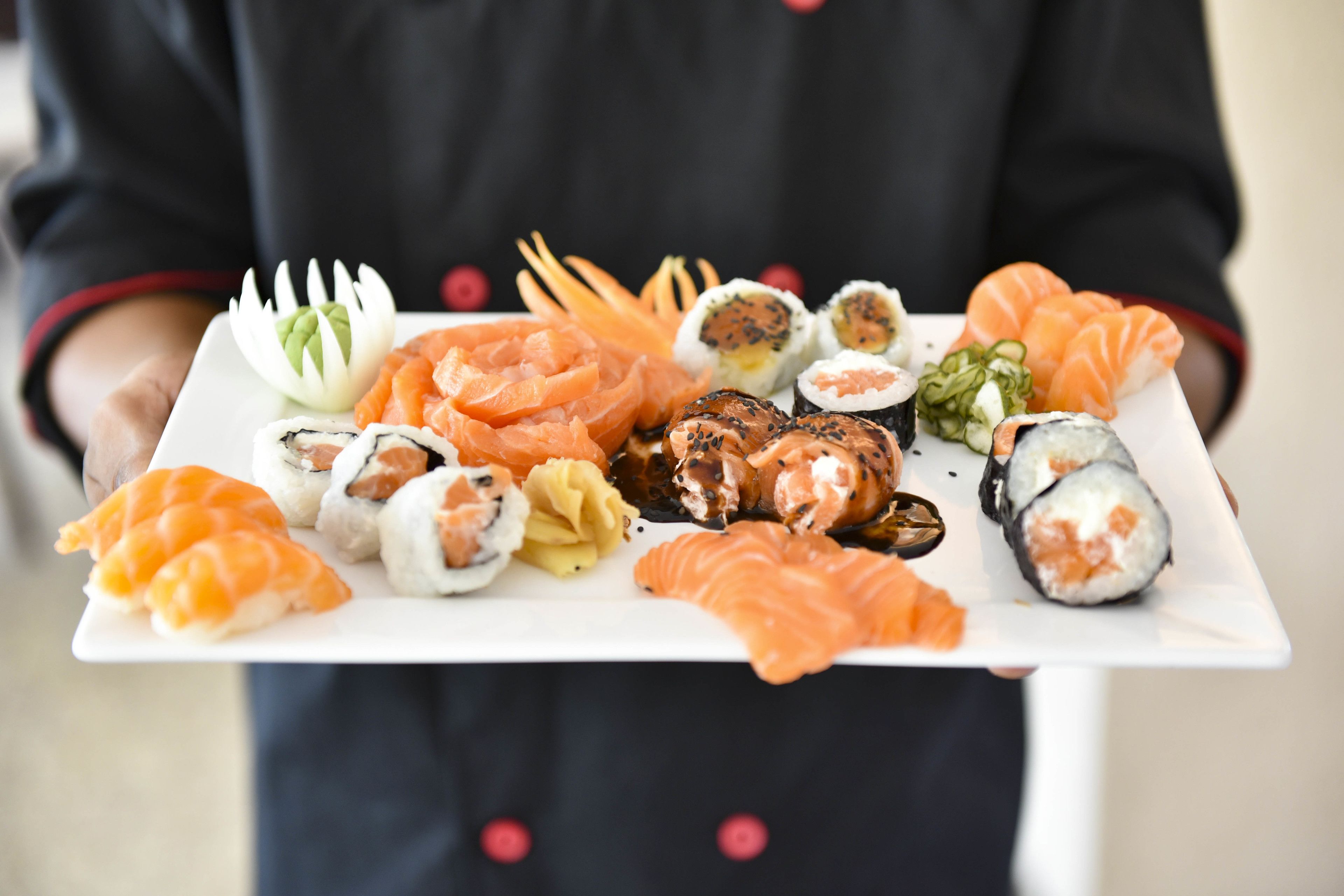 A person holding a tray with various sushi pieces.