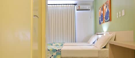 A room with two beds, a window with curtains, an air conditioning unit, and a wall with two paintings.