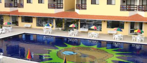 A hotel with a swimming pool, outdoor seating, and a colorful mural on the pool's surface.