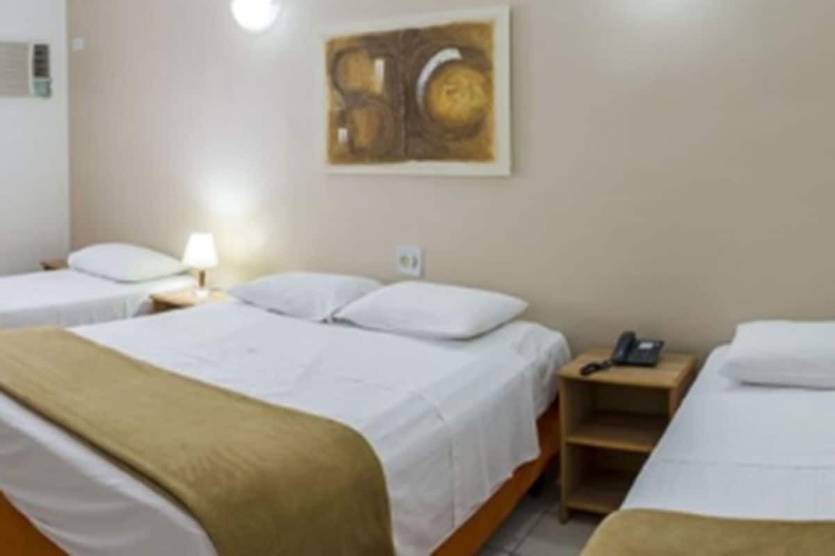 A hotel room with two single beds, a nightstand with a phone, and a wall-mounted artwork.