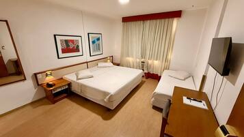 Quarto de hotel com uma cama grande, mesas de cabeceira, escrivaninha, uma cadeira, televisão e duas fotografias emolduradas na parede.