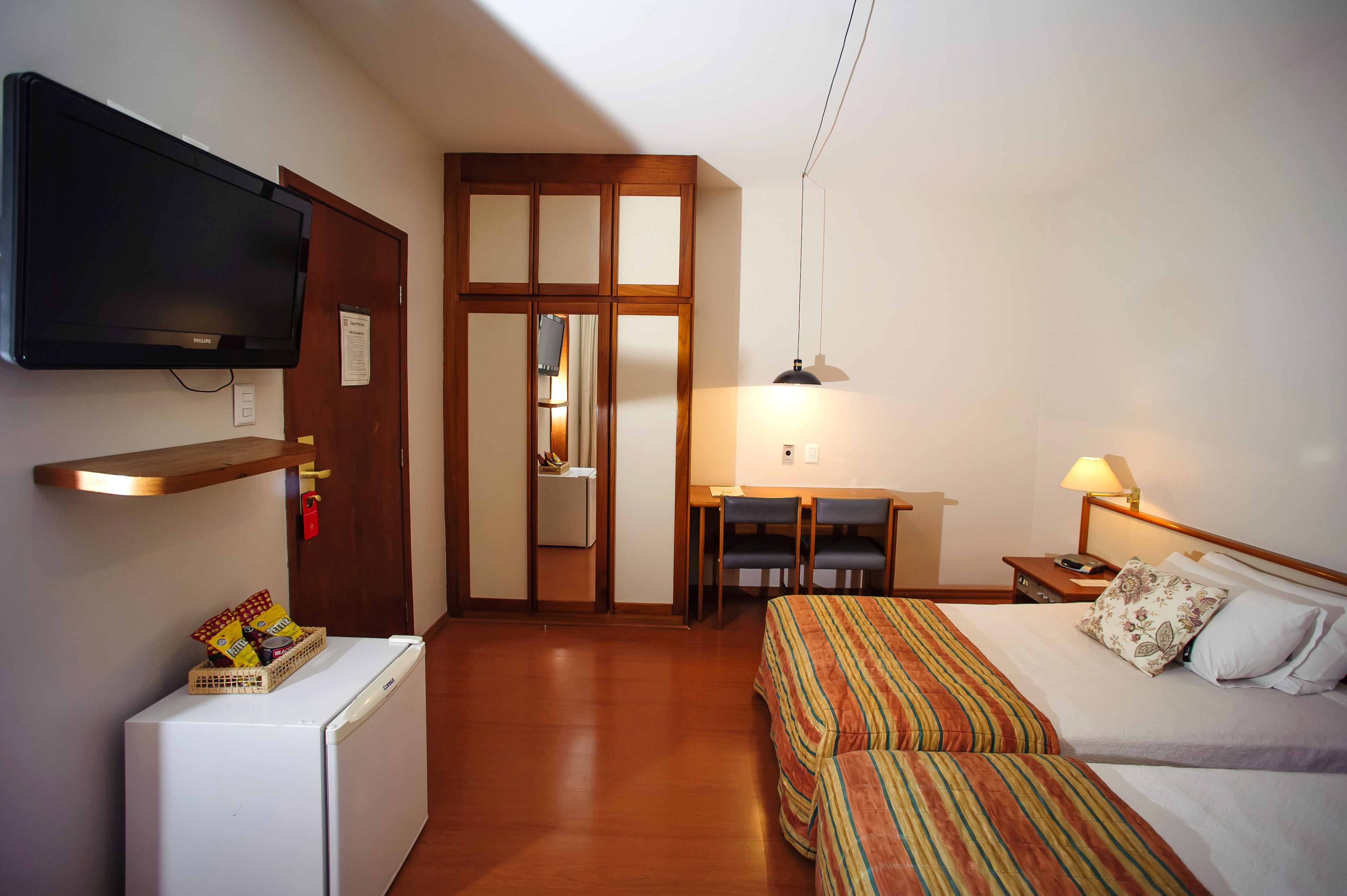 Una habitación de hotel pequeña con cama, escritorio, televisión y refrigerador.
