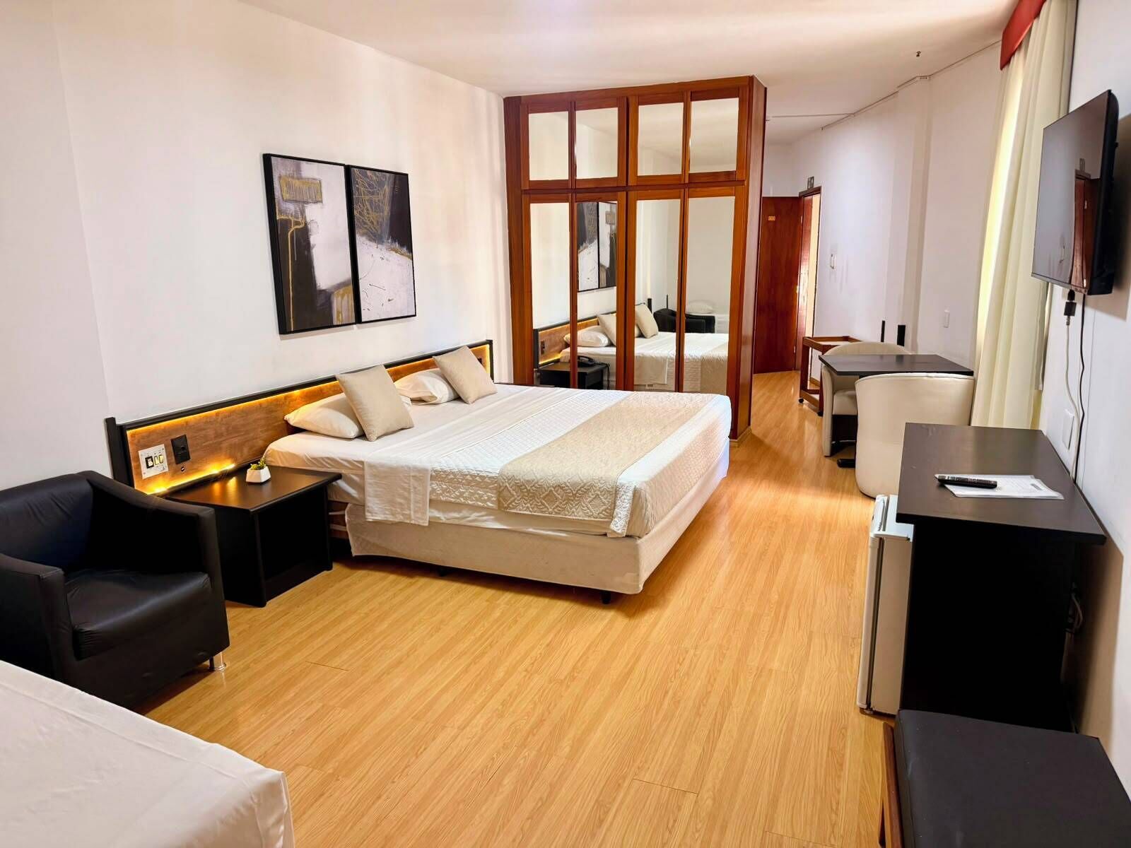 A hotel room with a large bed, a desk, a chair, a TV, and a wardrobe.