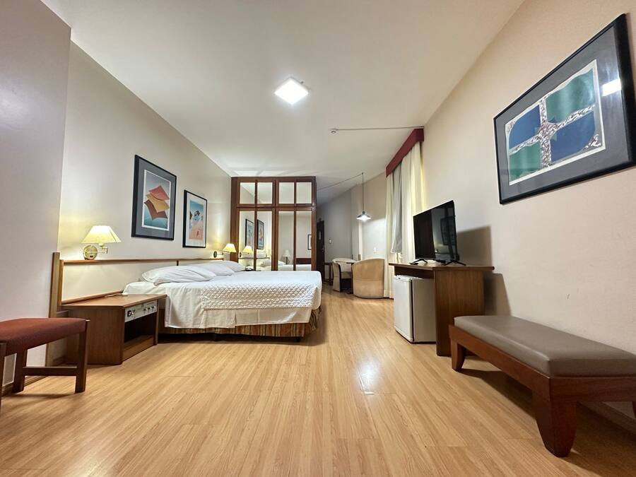 A hotel room with a bed, bedside tables, a desk, a chair, a TV, and a framed picture on the wall.