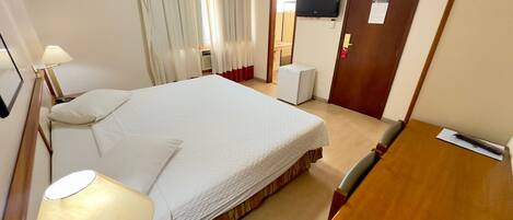 A hotel room with a bed, a desk, a chair, a TV, and a door.