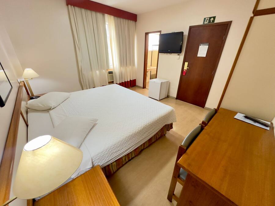 Una habitación de hotel con cama, escritorio, silla, televisor y puerta.
