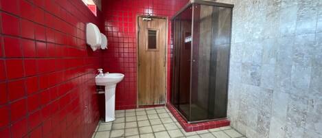 Un baño con paredes de azulejos rojos, un lavamanos blanco y una cabina de ducha de vidrio.