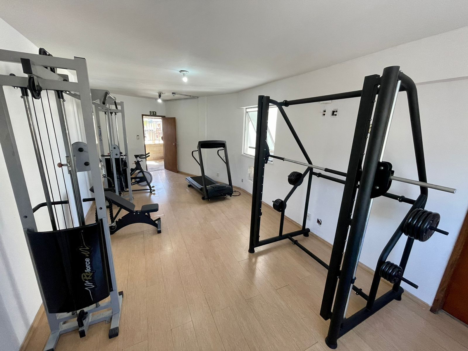 Un gimnasio en casa equipado con máquina de poleas, banca para press de banca, soporte para sentadillas, cinta de correr y banco de pesas.