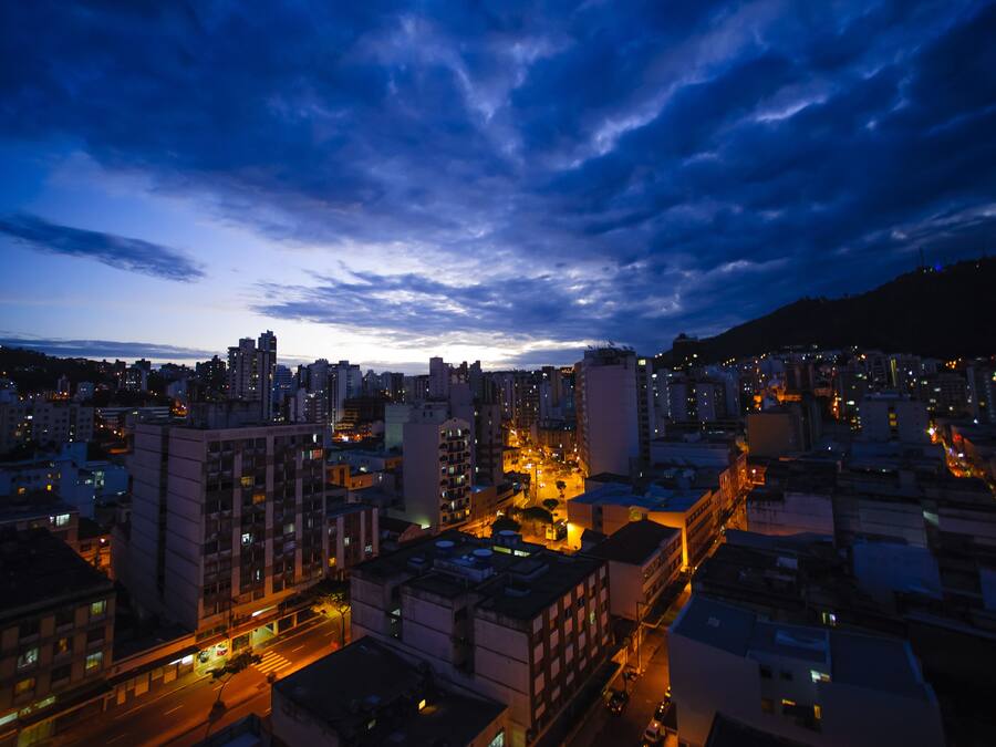 A cityscape at dusk with illuminated buildings and a cloudy sky.