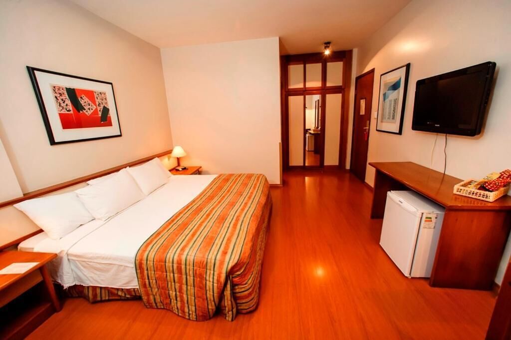 A hotel room with a bed, a desk, a television, and a refrigerator.