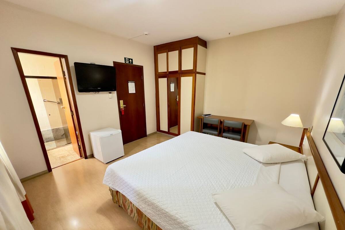 A hotel room with a bed, a desk, a chair, a television, and a door leading to a bathroom.