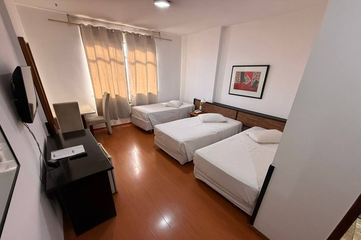 A hotel room with two single beds, a desk with a chair, a TV, and a window with curtains.