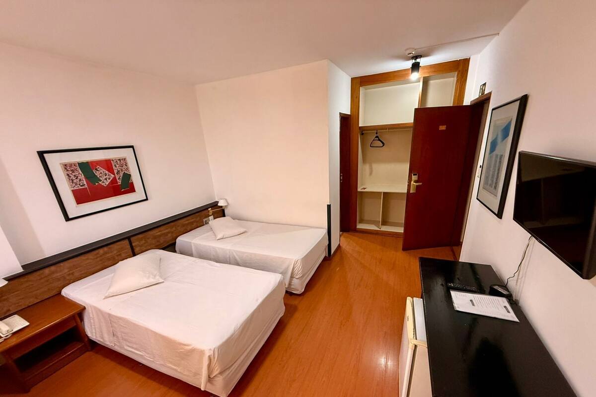 A hotel room with two beds, a desk with a computer, a TV, and a wardrobe.
