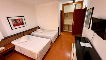 Ein Hotelzimmer mit zwei Betten, einem Schreibtisch mit Computer, einem Fernseher und einem Kleiderschrank.