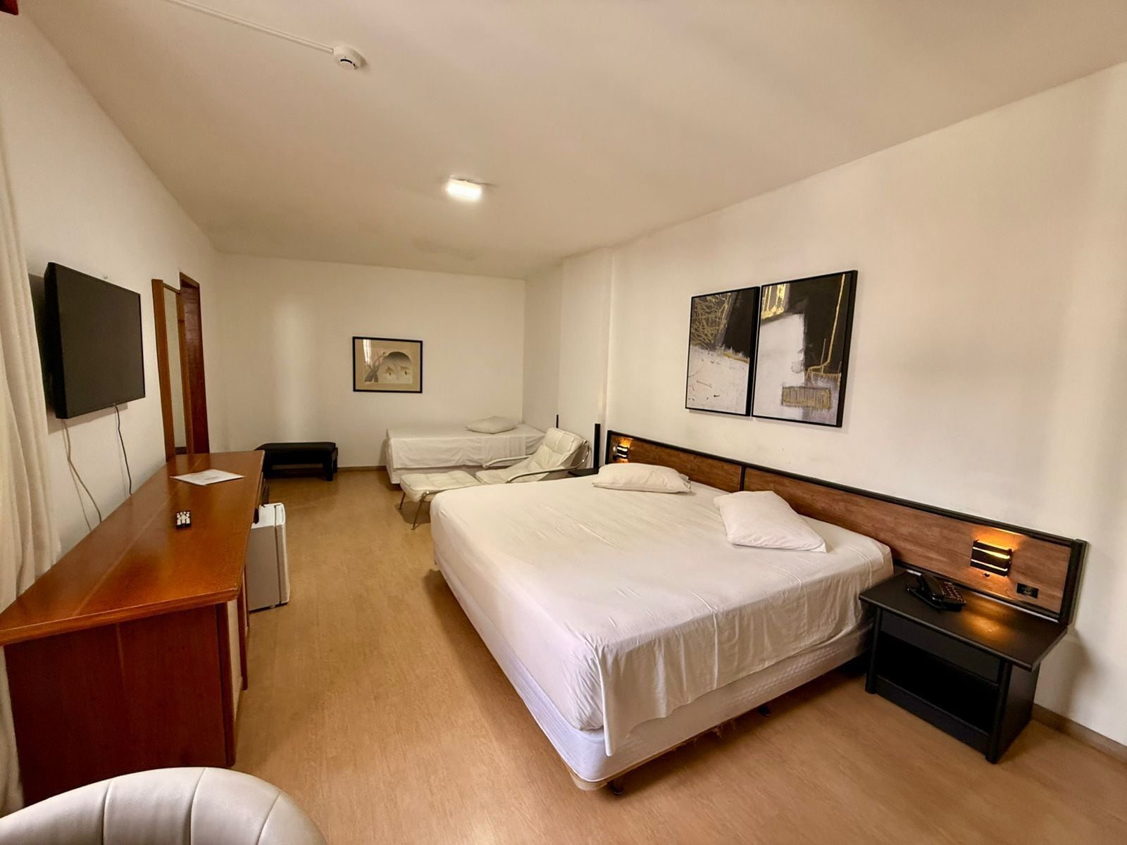 A hotel room with a bed, bedside table, desk, chair, and a flat-screen TV.