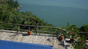 A wooden deck with potted plants overlooking a calm sea and distant mountains. - Pousada The Goldeneye (Porto Belo)