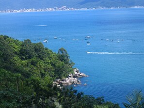 Une vue sur la côte, avec des bateaux, de la végétation et, au loin, les contours d’une ville.