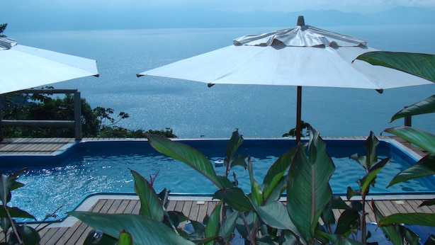 A pool area with two white umbrellas and a view of the sea. - Pousada The Goldeneye (Porto Belo)
