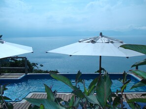 Un espace piscine agrémenté de deux parasols blancs et offrant une vue sur la mer.