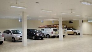 A parking garage with multiple cars parked under white pillars and ceiling fans. - Alves Hotel (Marilia)
