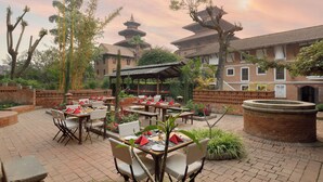 An outdoor dining area with tables and chairs, surrounded by brick walls and greenery. - Hotel Himalaya Kathmandu - Your Business & Leisure Retreat (Lalitpur)