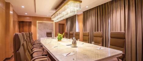 A conference room with a long table, leather chairs, a chandelier, and a curtain backdrop.