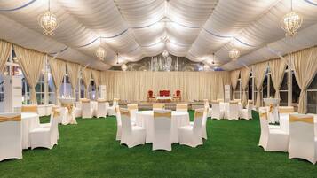 Un espacio para eventos con carpas, mesas redondas y sillas, un escenario con sillas rojas y candelabros.