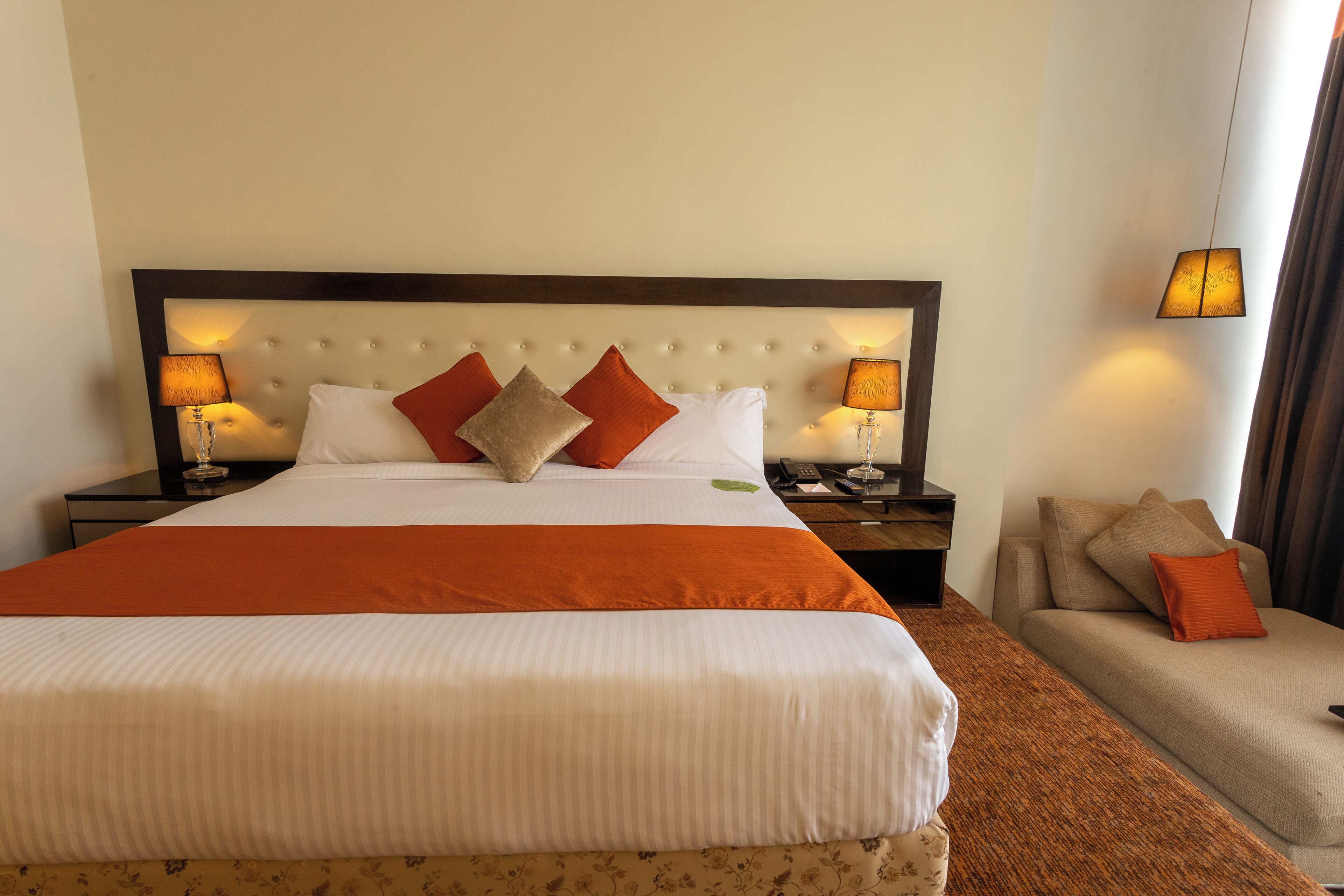 A hotel room with a large bed, two bedside tables with lamps, a sofa, and a headboard with a tufted design.