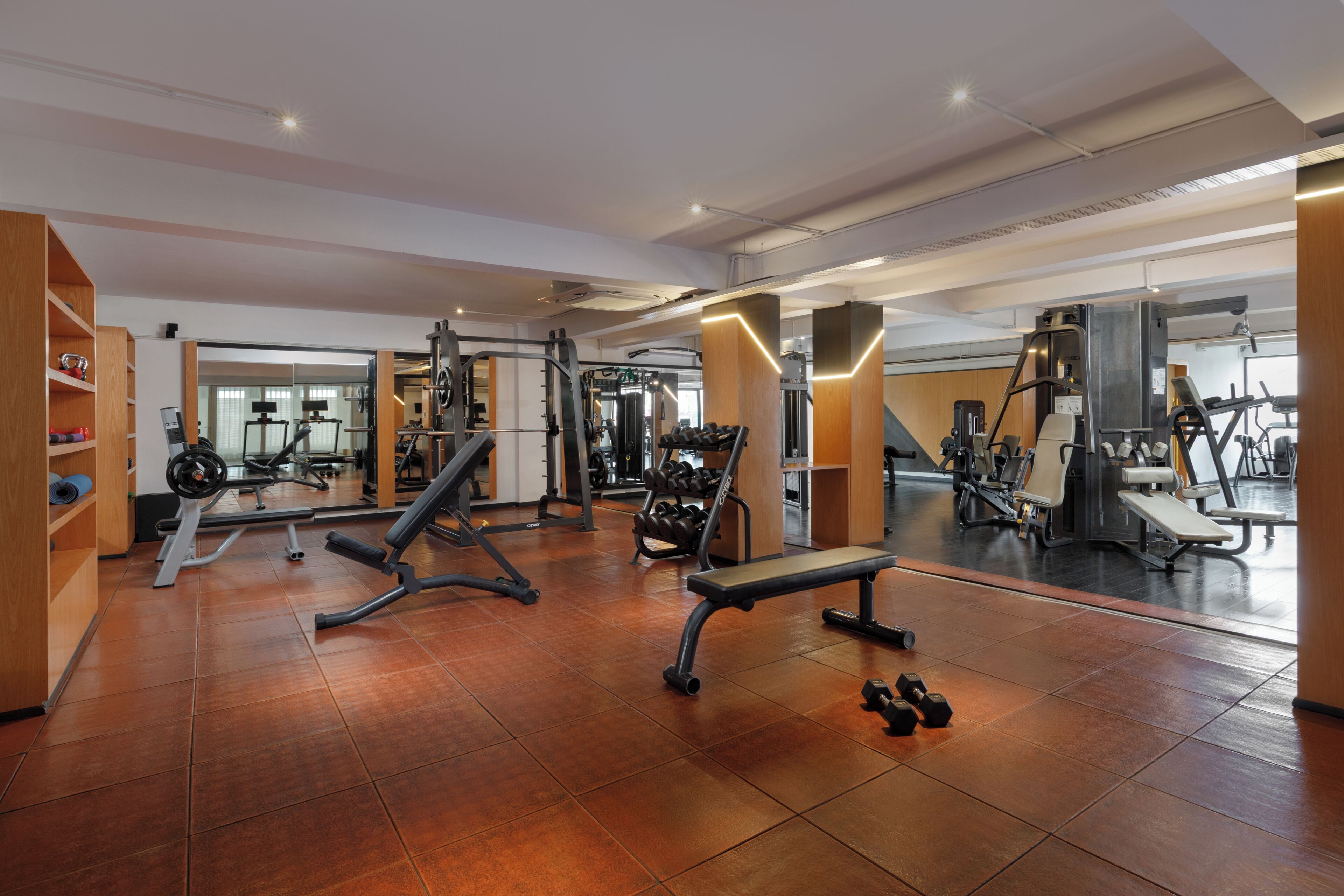 A gym with various exercise equipment, wooden flooring, and a mirrored wall.