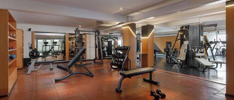 A gym with various exercise equipment, wooden flooring, and a mirrored wall.