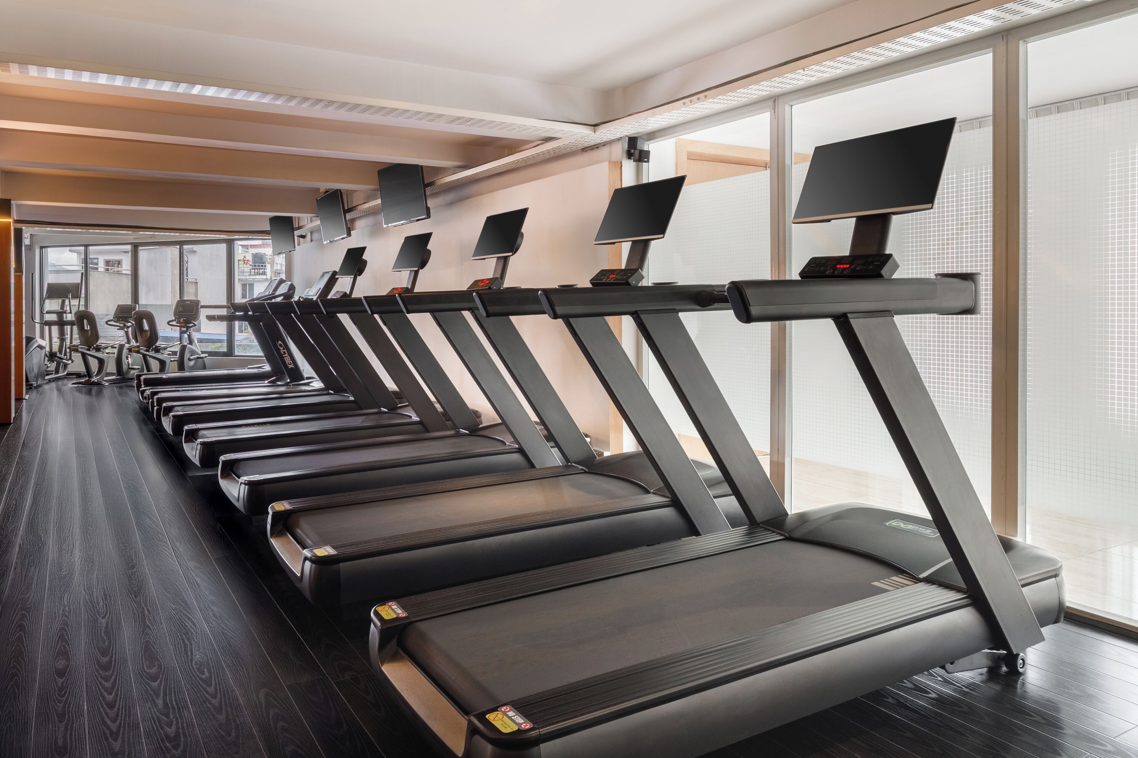 A gym with multiple treadmills, exercise equipment, and large windows.