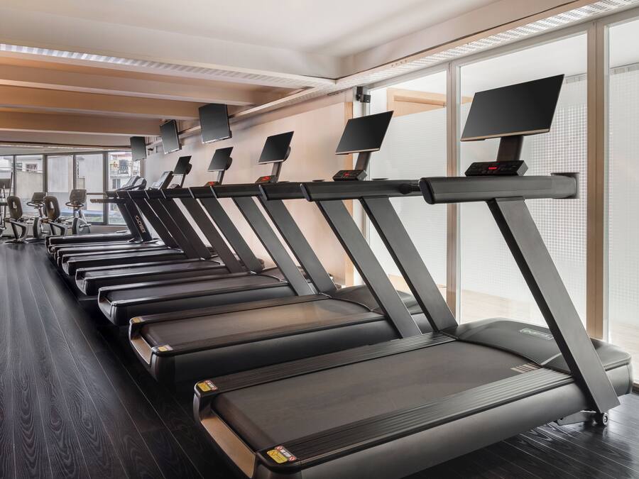 Un gimnasio con varias cintas de correr, equipo de ejercicio y amplias ventanas.
