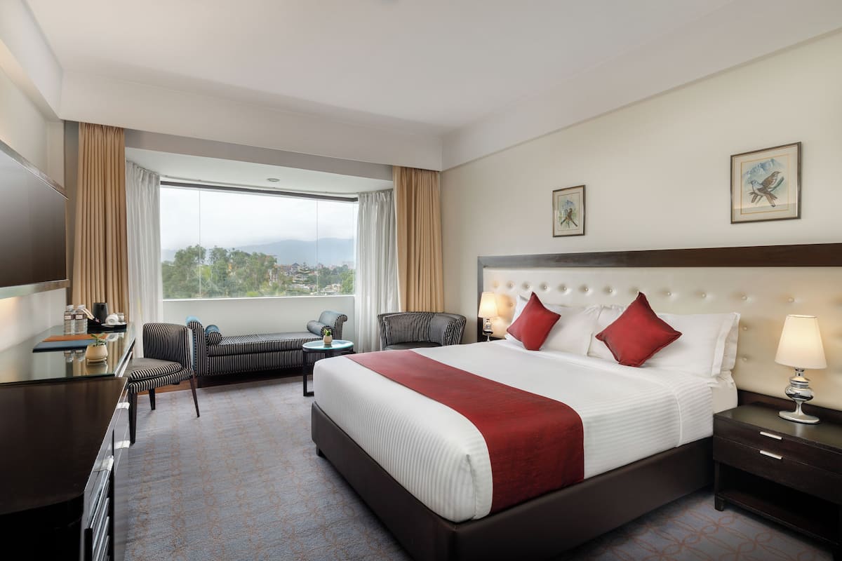 Habitación de hotel con una cama grande, un escritorio, una silla, un sofá y vistas al exterior.