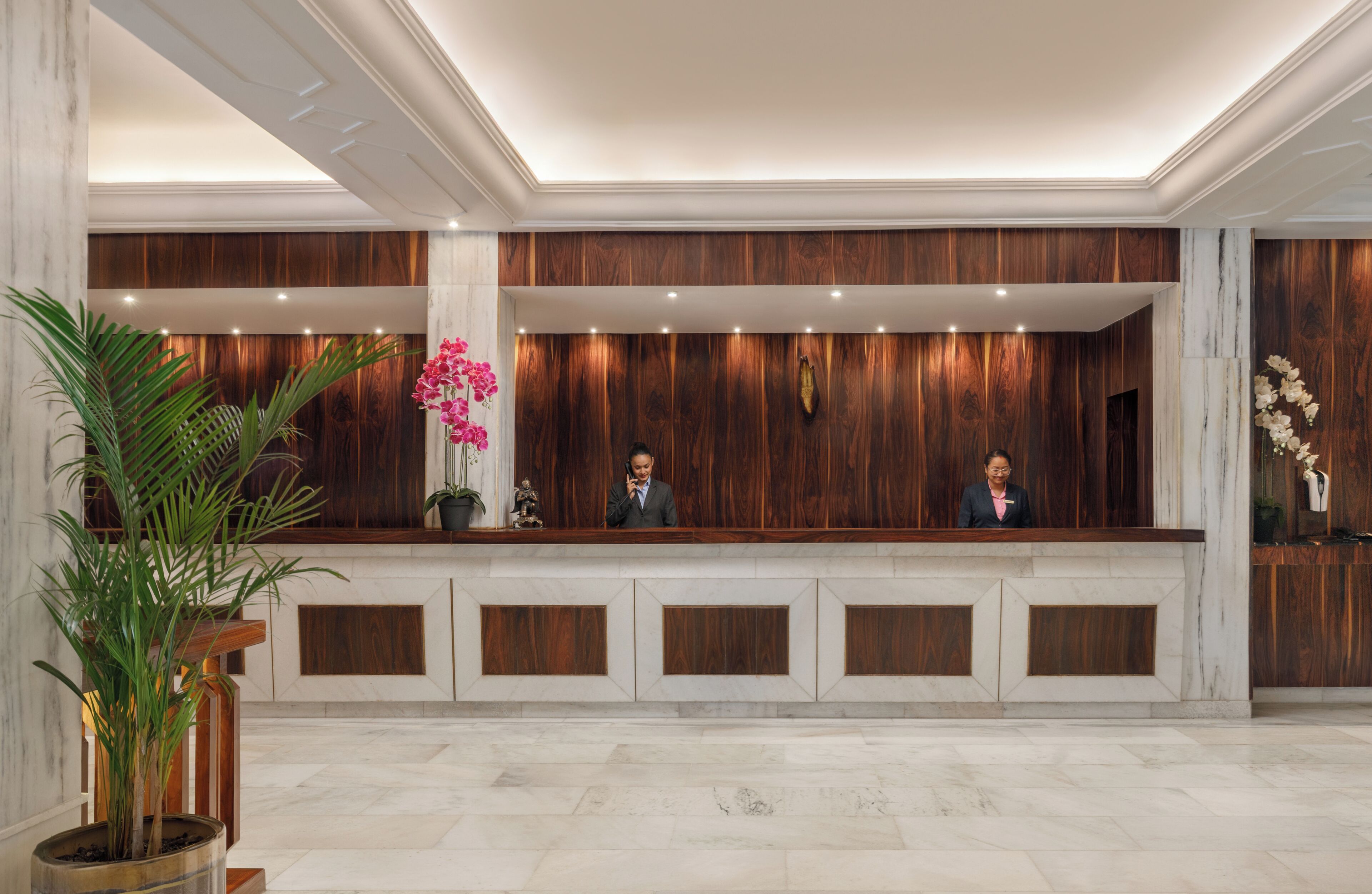 A reception desk with wooden paneling, marble flooring, and potted plants.