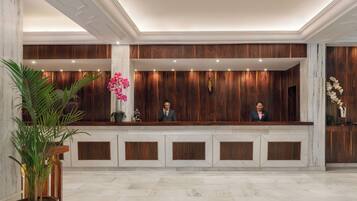 A reception desk with wooden paneling, marble flooring, and potted plants.