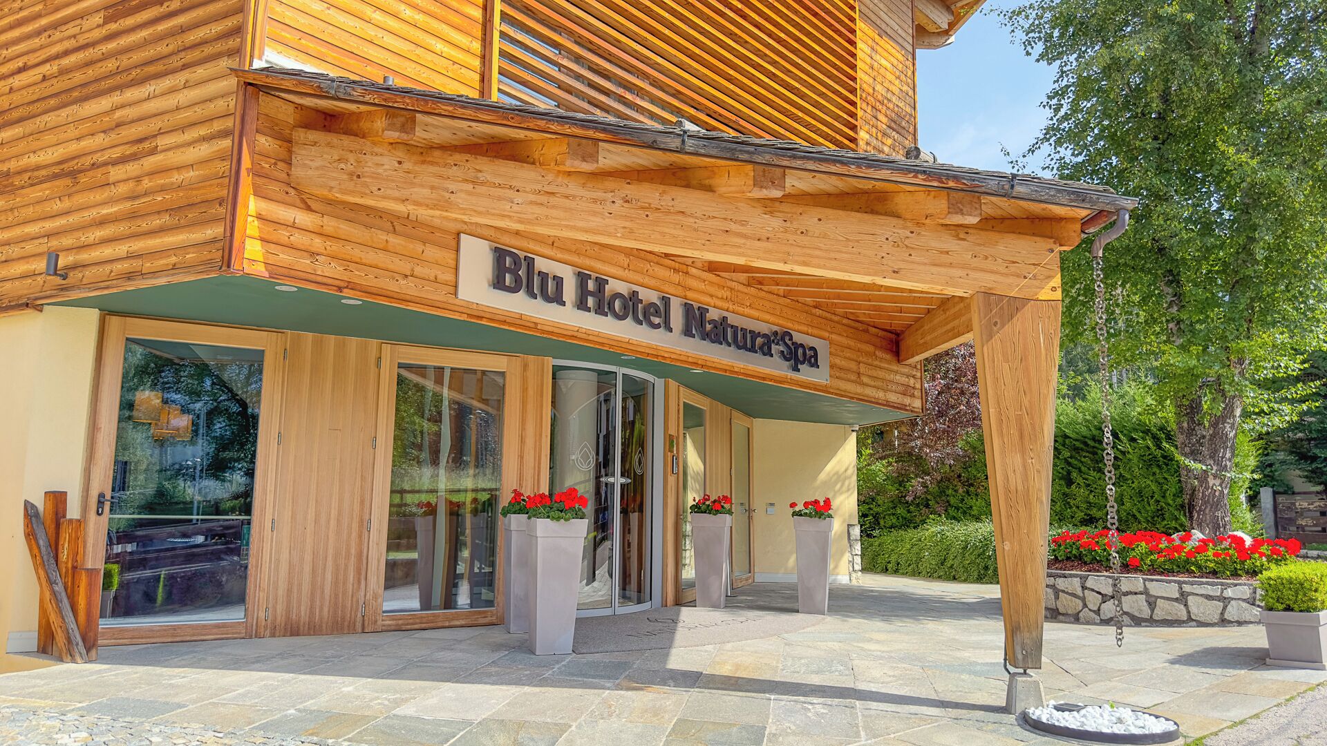 Ein Hotel Eingang mit einer Holzfassade, großen Glasüren und einem Schild mit der Aufschrift 'Blu Hotel NaturaSpa'.